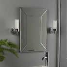 Two wall lights illuminate a framed mirror above a bathroom sink and faucet.