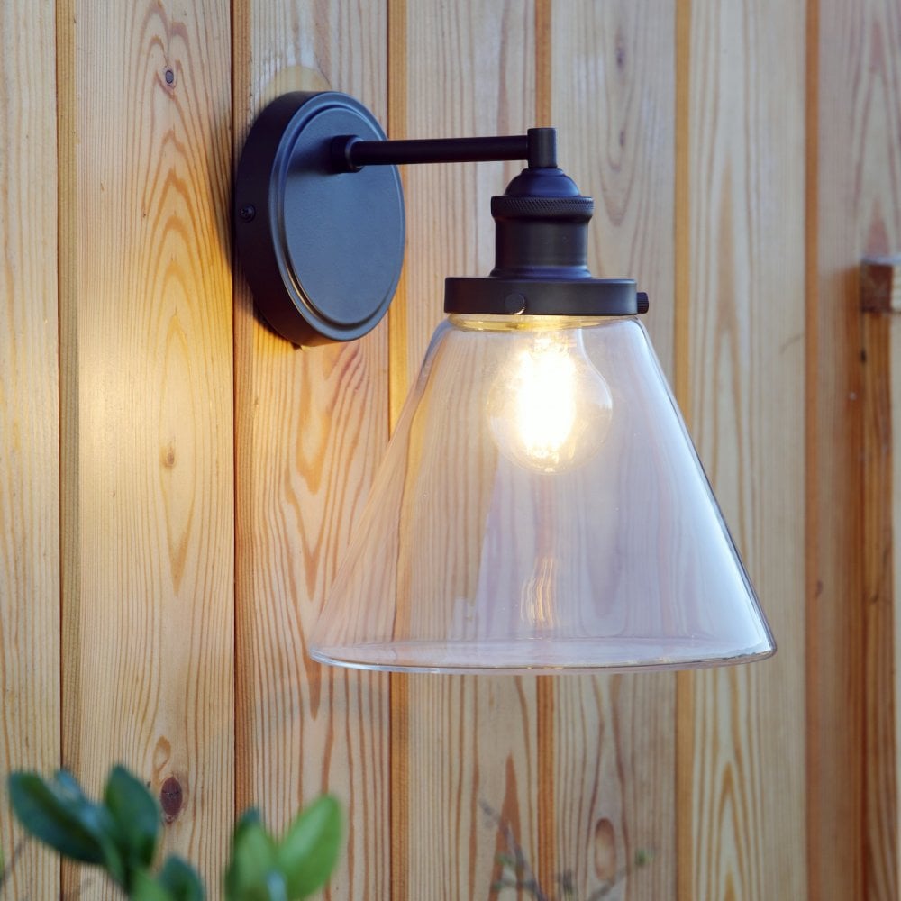 Vintage outdoor wall light with a black fixture and clear conical glass shade, illuminated on wood.