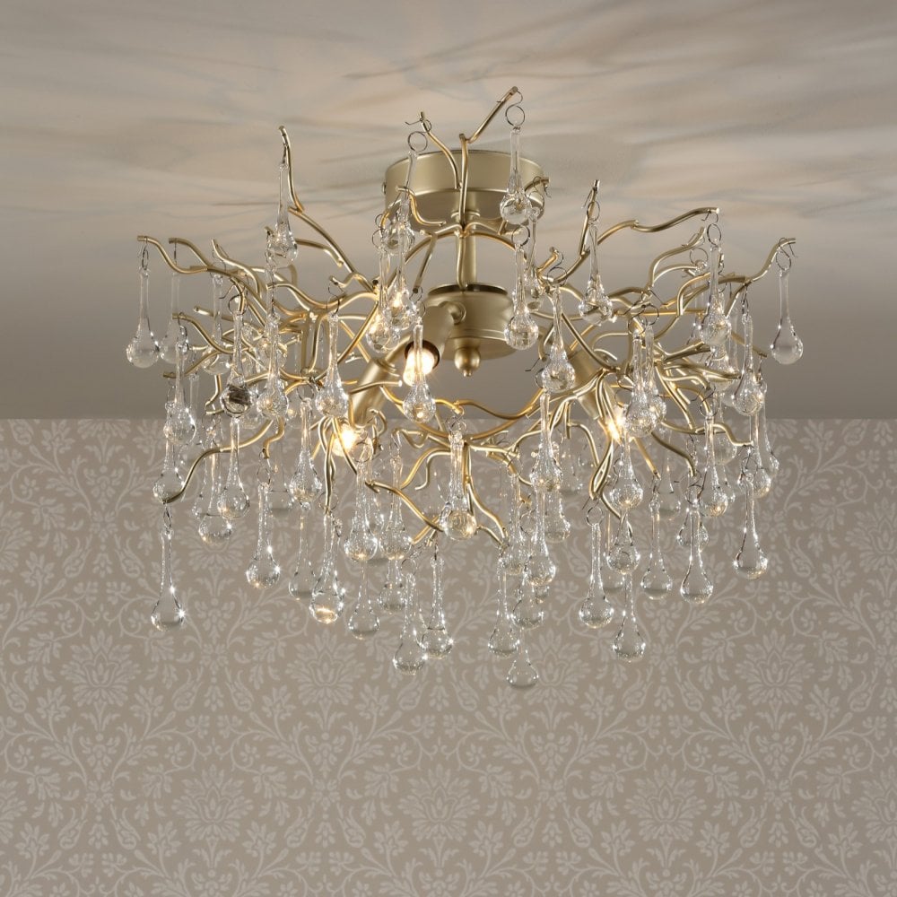 A close-up of a gold chandelier with hanging glass droplets against a patterned wall.