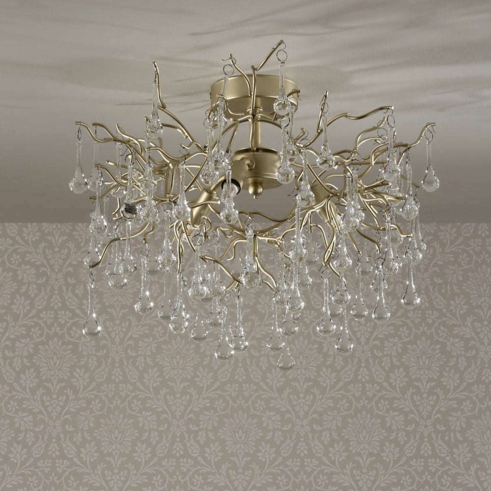 A gold chandelier with glass droplets suspended from a ceiling, illuminating a patterned wall.