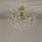 A gold chandelier with glass droplets suspended from a ceiling, illuminating a patterned wall.