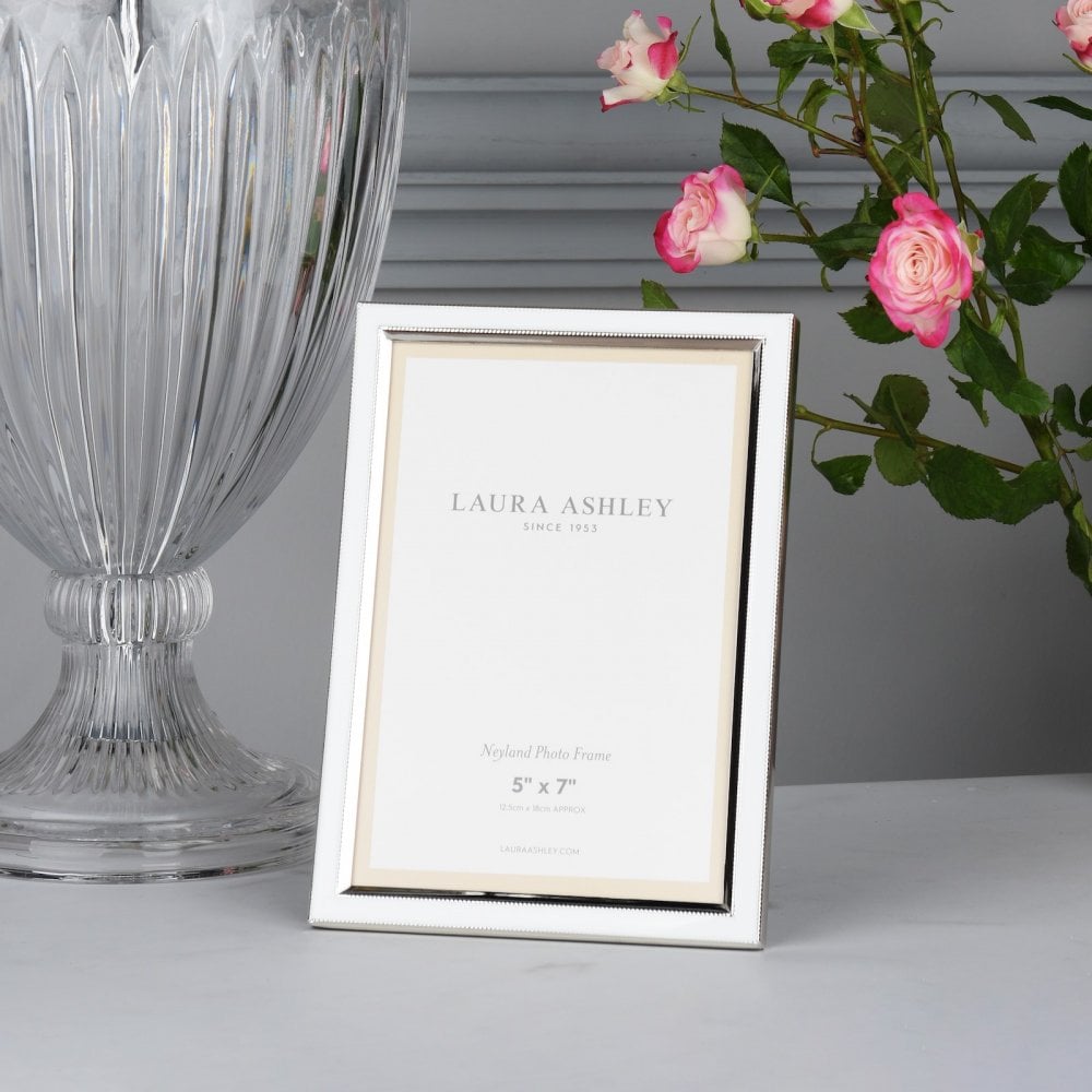 A shiny silver Laura Ashley 5" x 7" photo frame with a clear glass vase and pink roses.