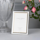 A shiny silver Laura Ashley 5" x 7" photo frame with a clear glass vase and pink roses.