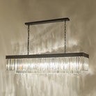 A rectangular chandelier with a black frame and crystal rods illuminating a wall.