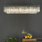 A rectangular crystal chandelier hanging above a dark wooden console table with fruit.