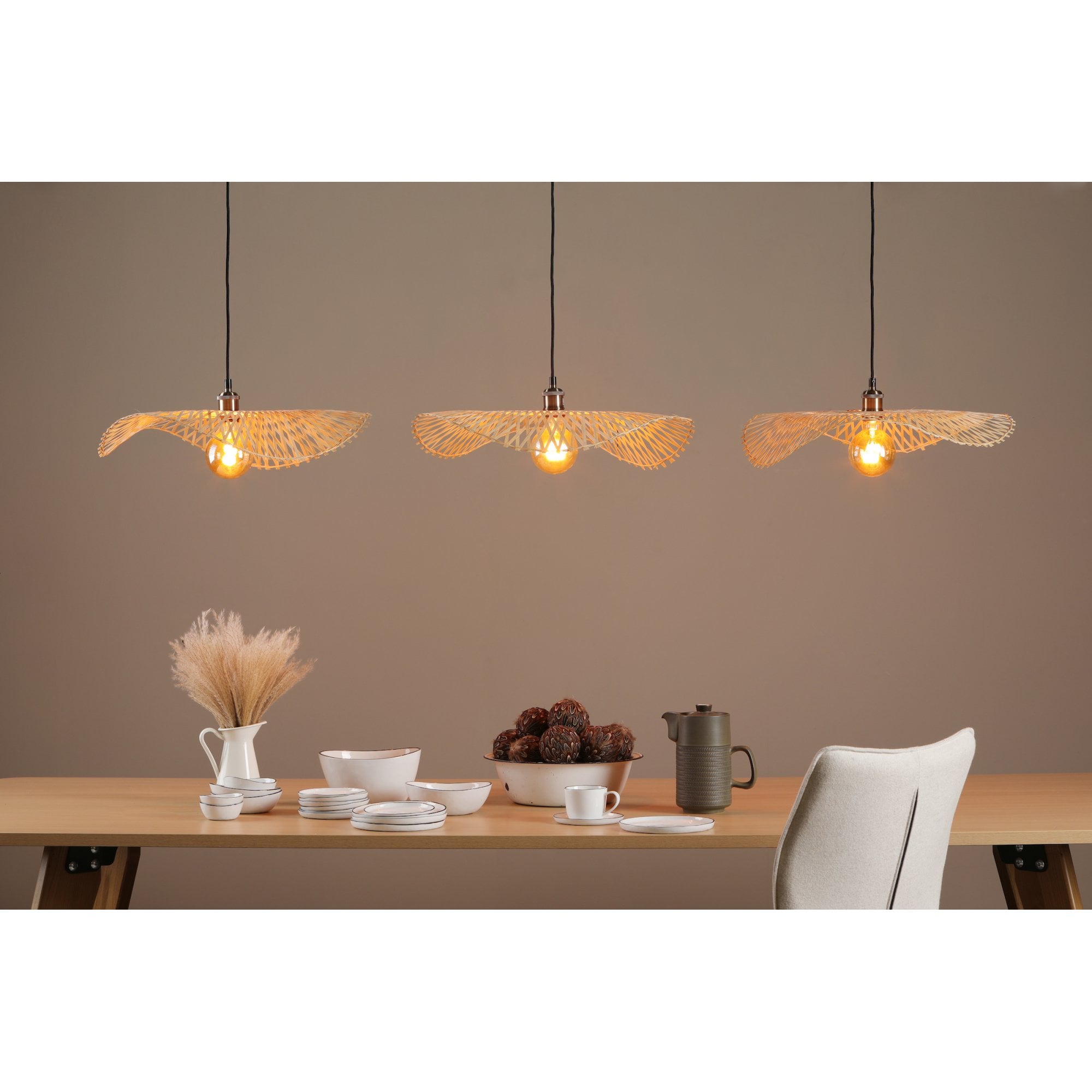 Three ceiling lights over a dining table with place settings, bowls, and a jug with pampas grass.