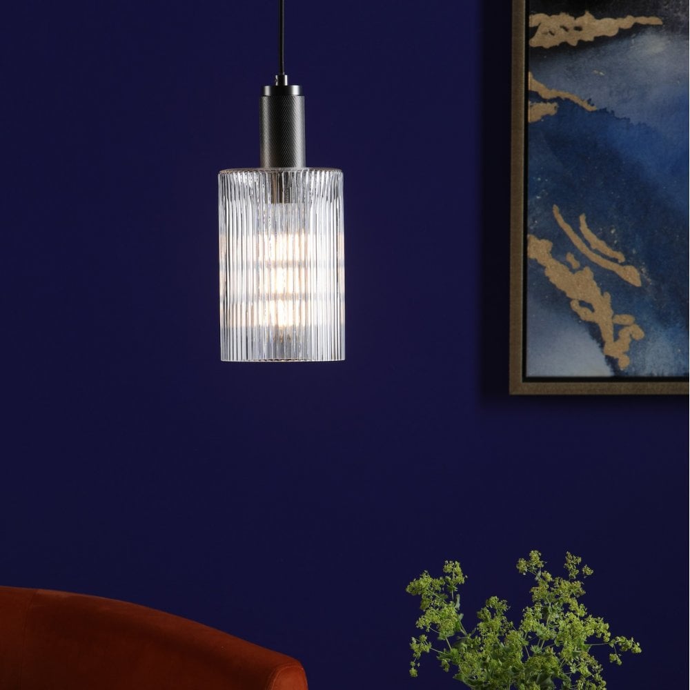 An illuminated ribbed glass and antique brass pendant light in a blue room.