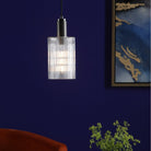An illuminated ribbed glass and antique brass pendant light in a blue room.
