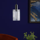A ribbed glass and antique brass pendant light in a blue room, not illuminated.