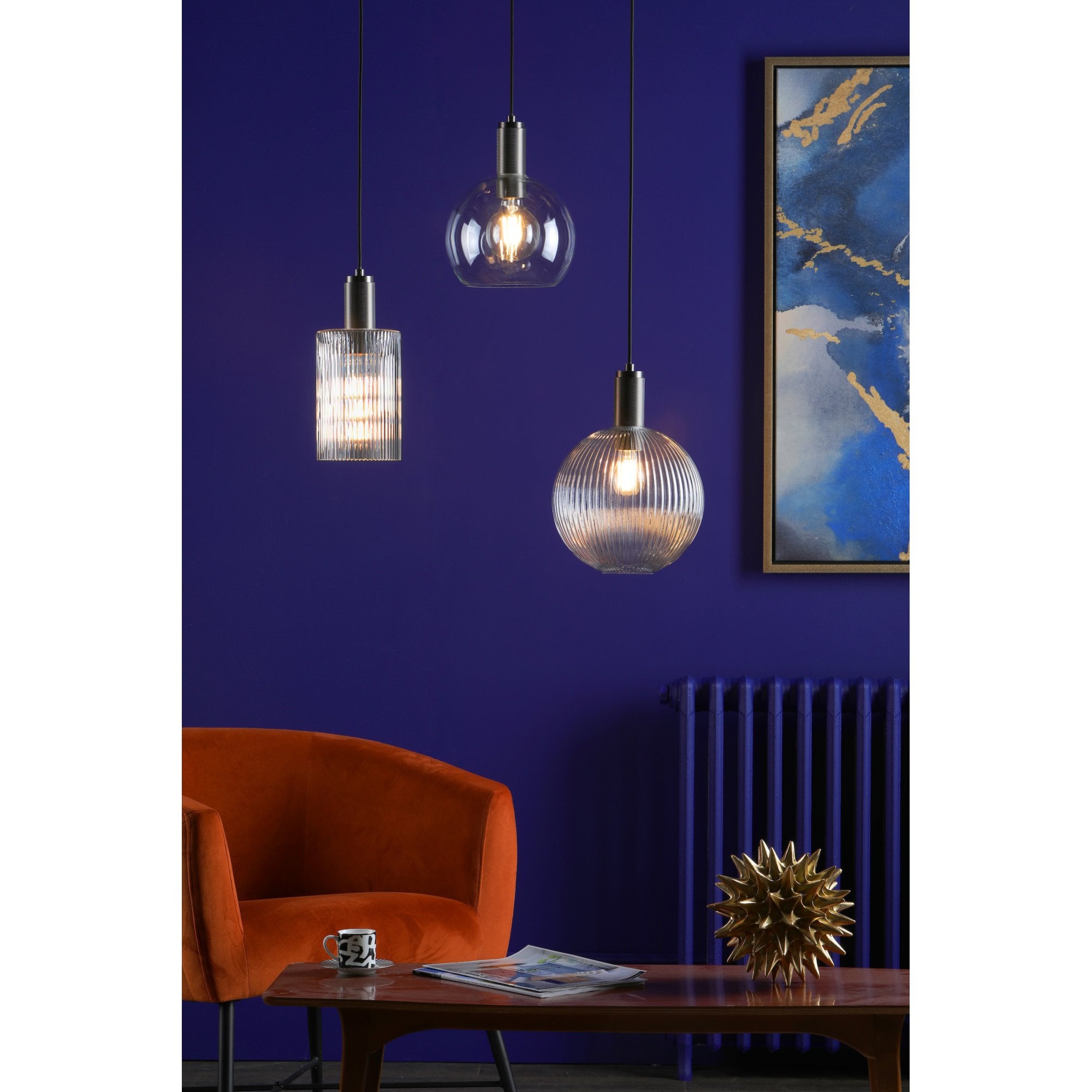 Three pendant lights, two illuminated, in a blue room with an orange chair.