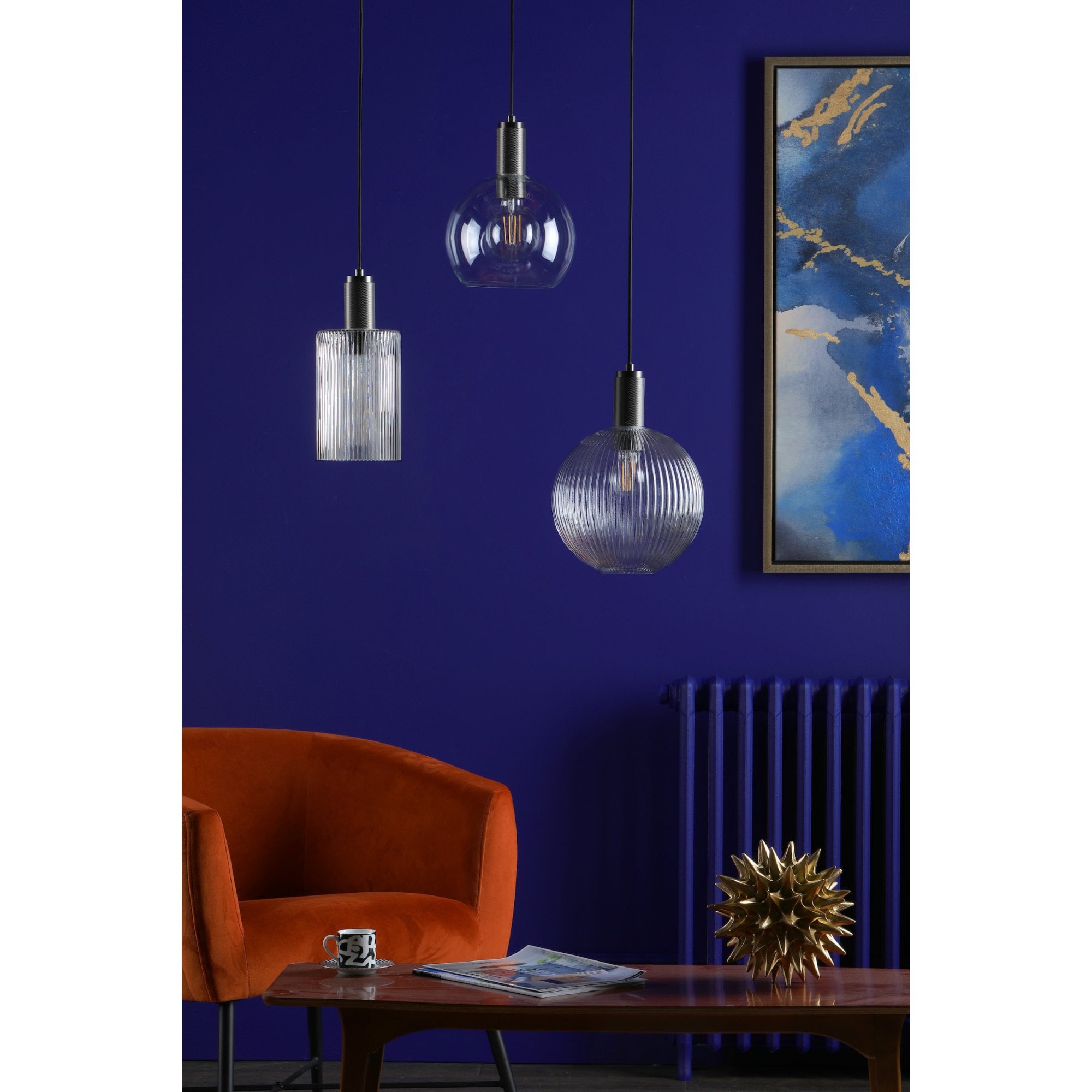 Three pendant lights, none illuminated, in a blue room with an orange chair.