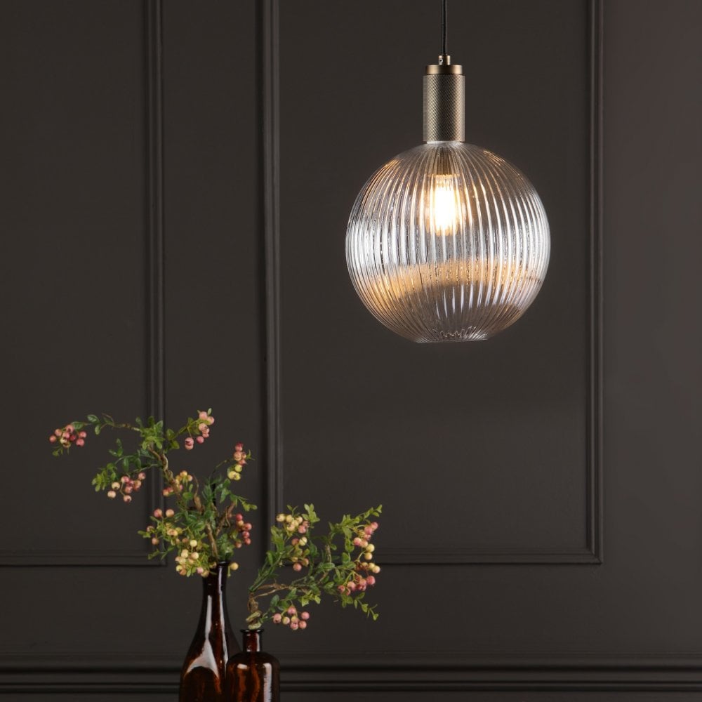 A ribbed glass globe pendant light illuminates a dark room with a floral arrangement.