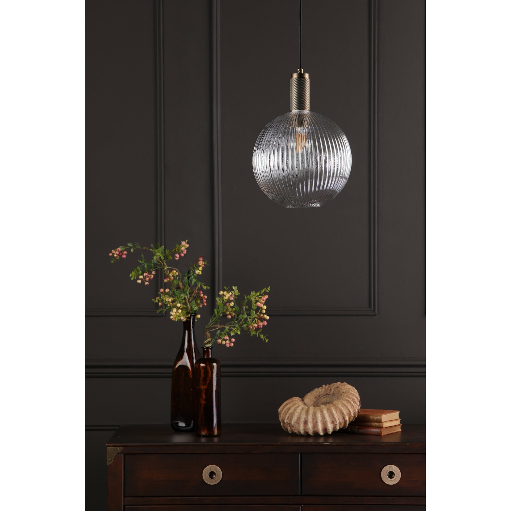 A ribbed glass globe pendant light hangs above a dark wooden dresser with decor.