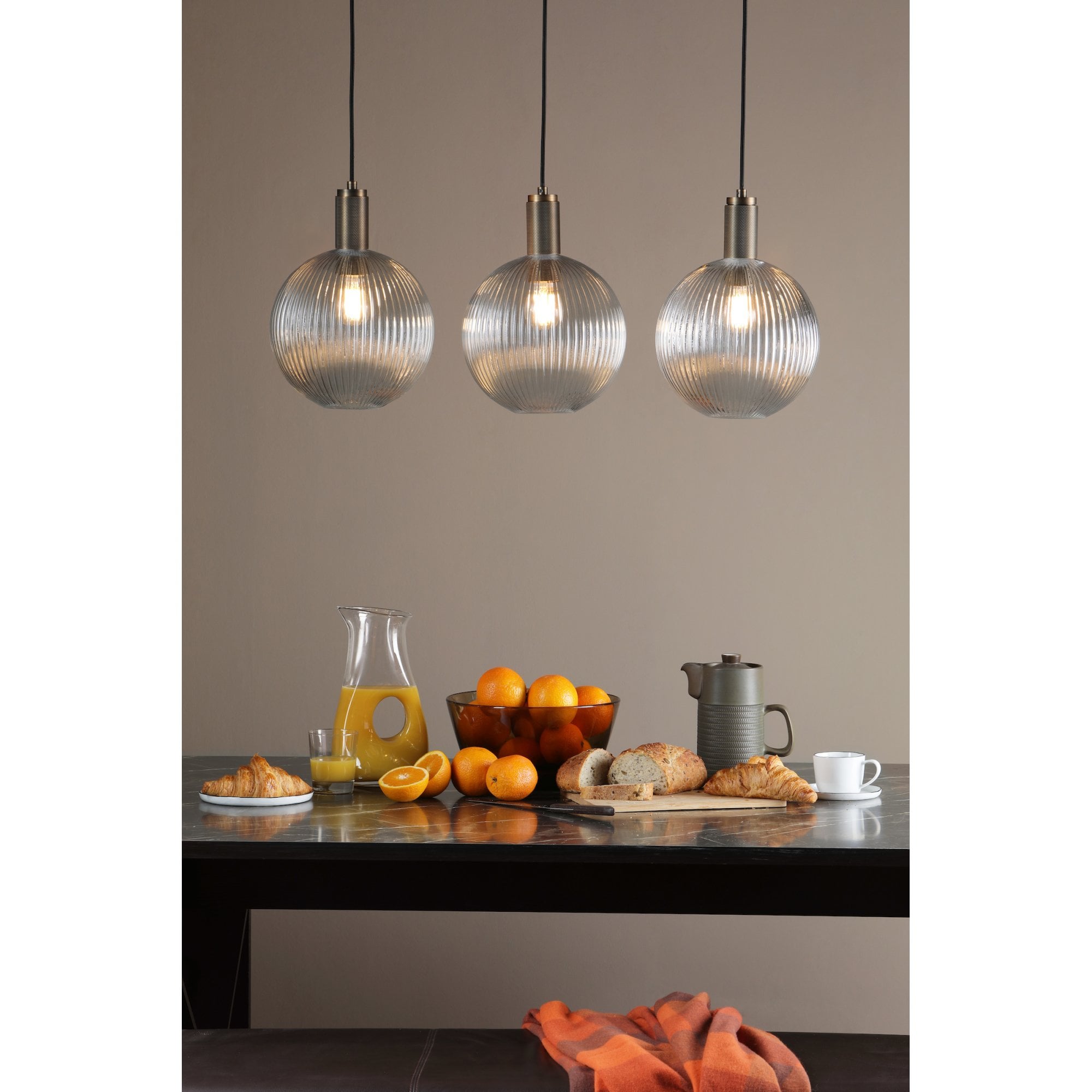 Three ribbed glass globe pendant lights illuminate a breakfast table setting.