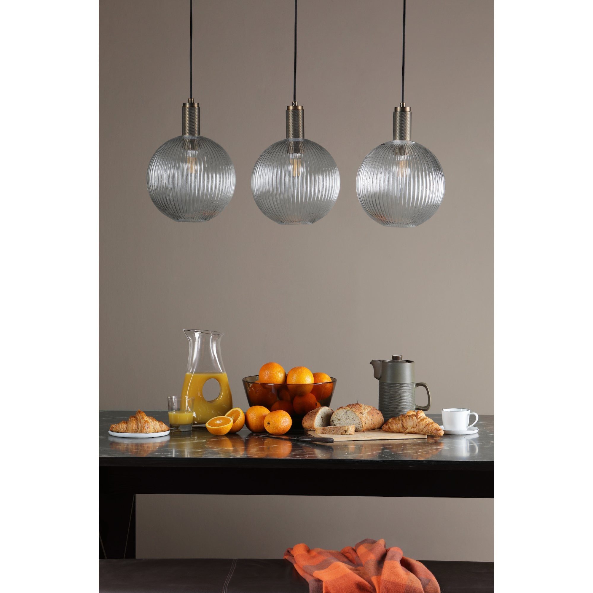 Three ribbed glass globe pendant lights illuminate a breakfast spread on a table.