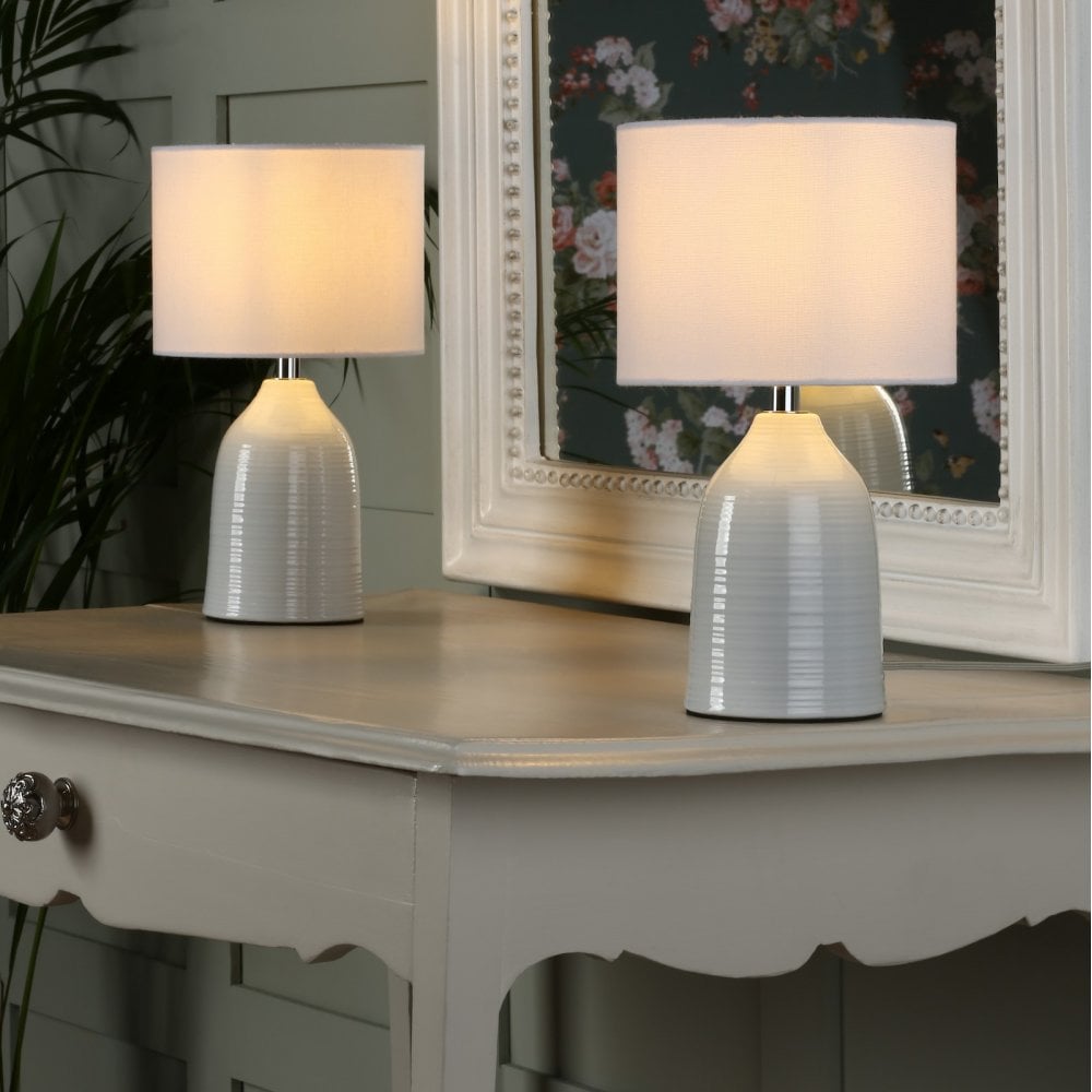Two white ceramic table lamps with drum shades on a light grey console table.