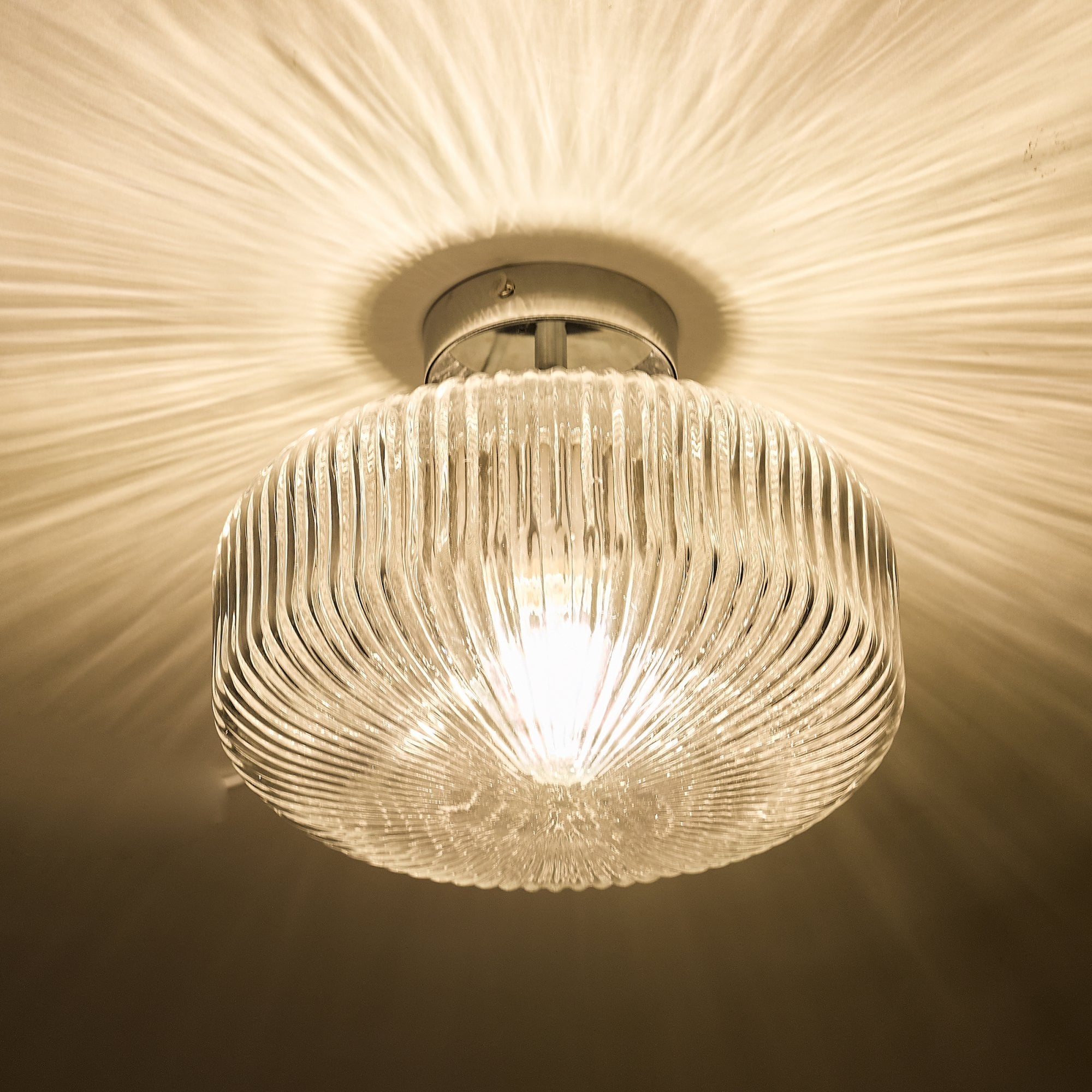 A close-up, bottom-up view of the ribbed glass flush ceiling light, lit.