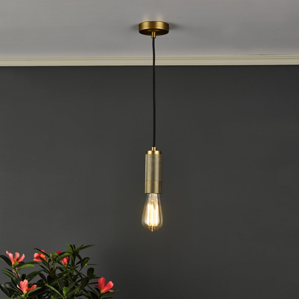 A brass pendant light with an exposed bulb hanging in a room with a dark grey wall.