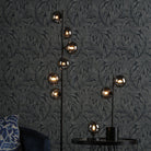 Floor and table lamps with smoked glass spheres illuminating a dark botanical wallpaper.
