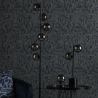 Floor and table lamps with smoked glass spheres in a room with dark botanical wallpaper.