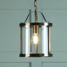 A vintage style pendant light with a clear glass shade and antique brass finish against a teal wall.