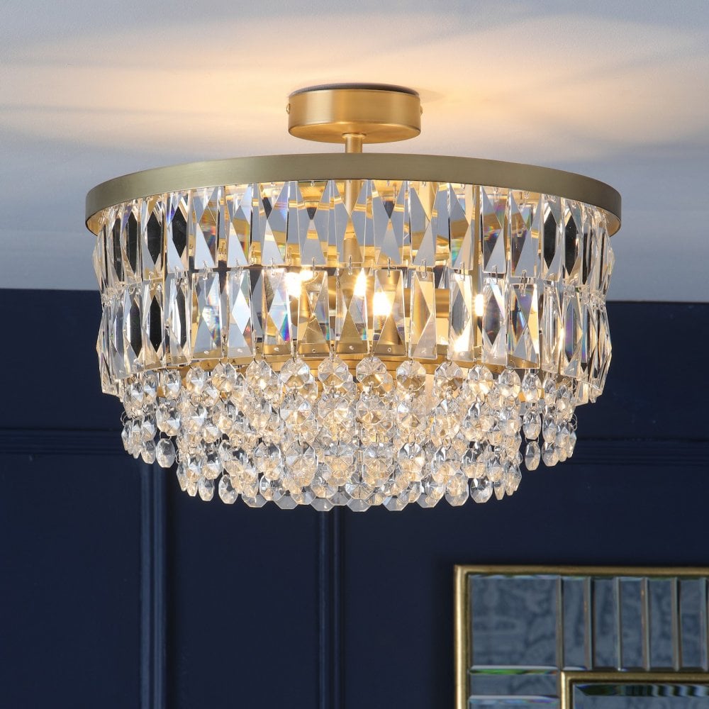Crystal chandelier with warm light against a dark blue wall and gold mirror.