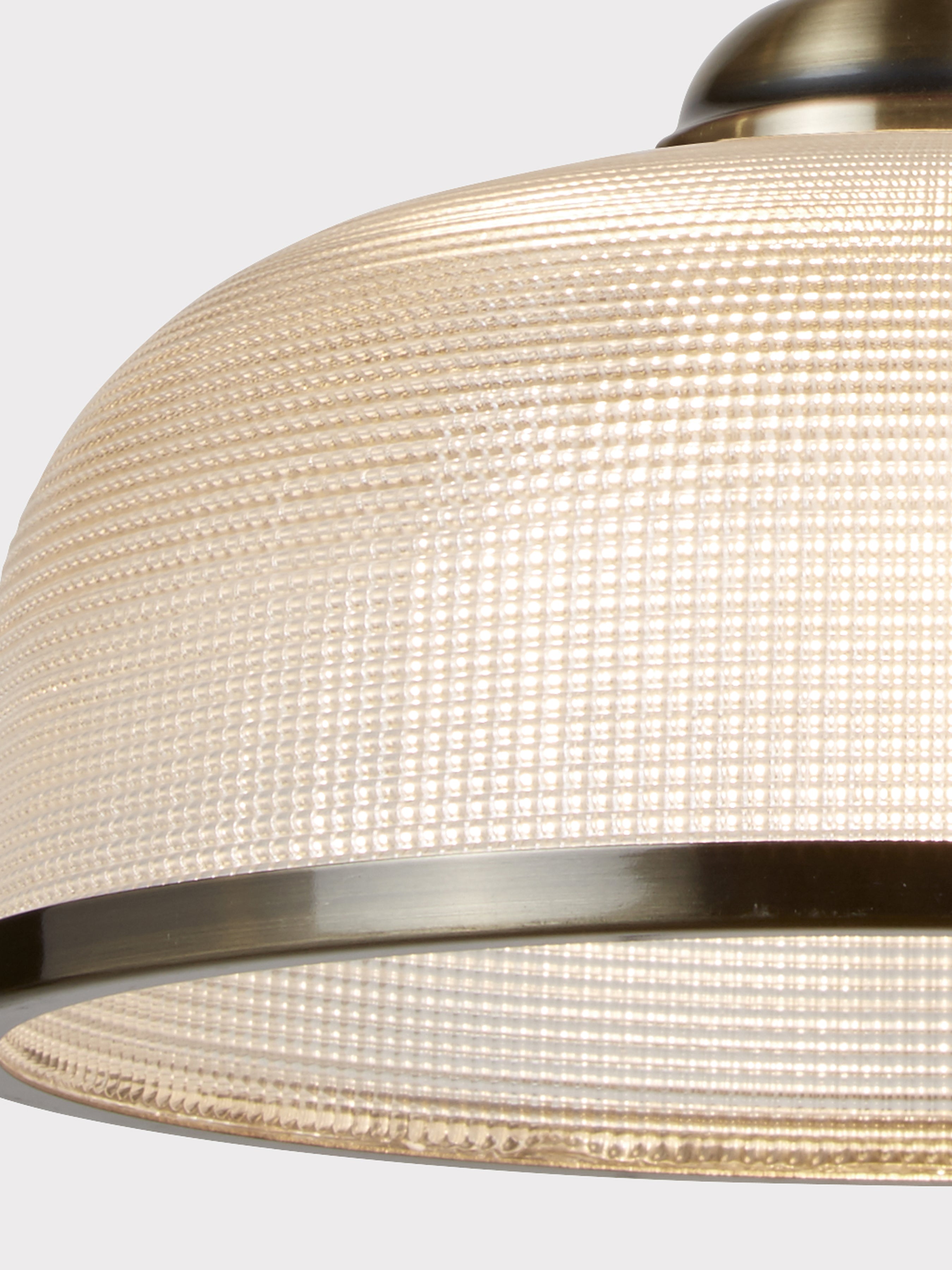 A close-up of a pendant lamp's textured glass dome shade with a brass-colored trim.