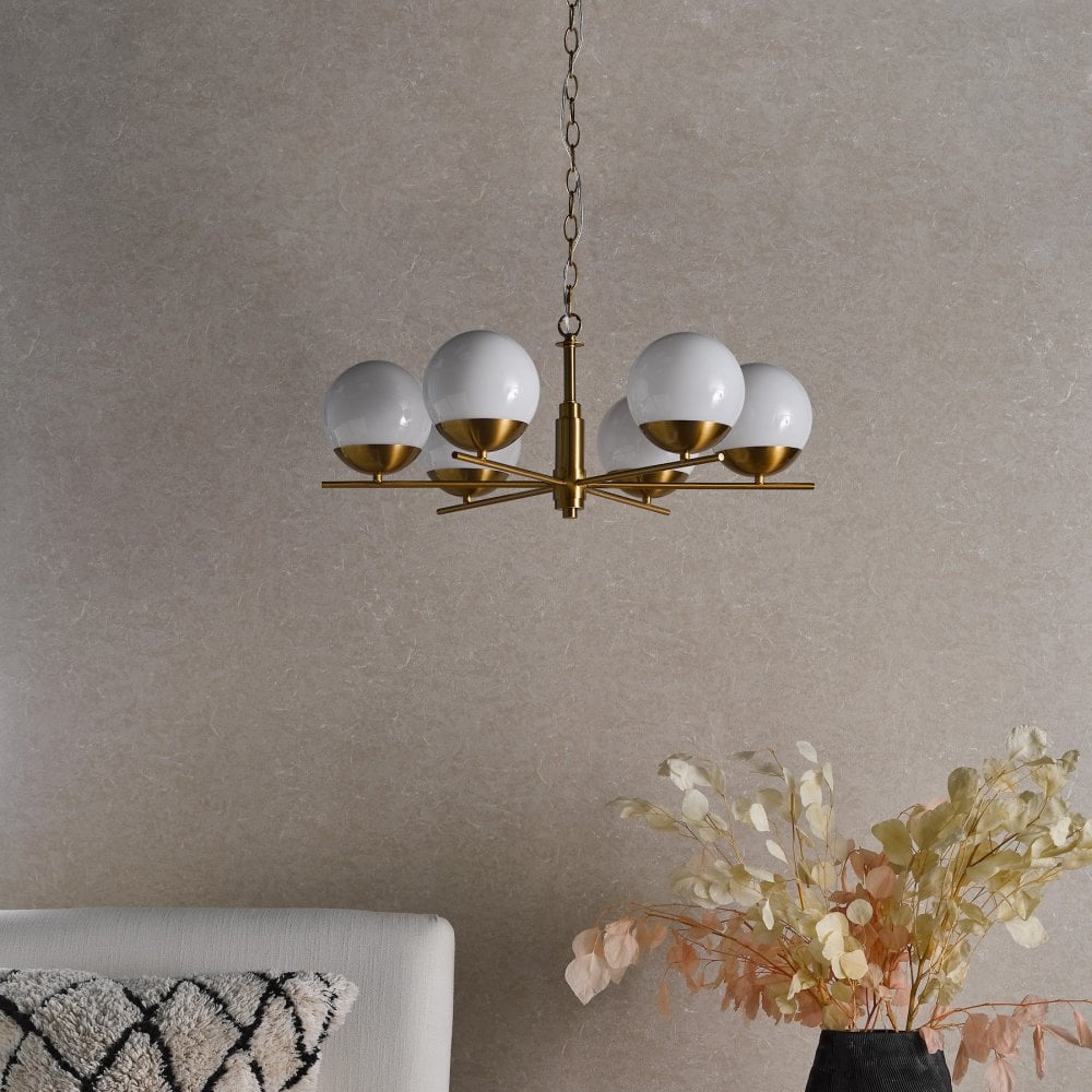 A modern brass chandelier with six white globe lights, illuminating a room with soft light.