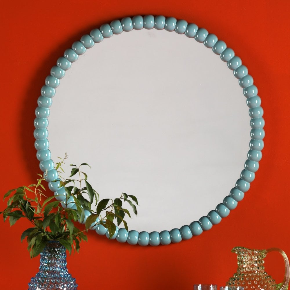 Round mirror with a light blue beaded frame hanging on an orange wall.