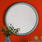 Round mirror with a light blue beaded frame hanging on an orange wall.