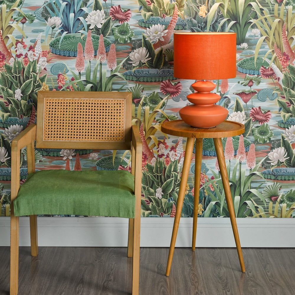 Orange table lamp on a side table next to a chair, complementing the floral wallpaper.