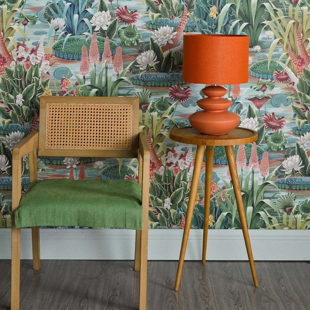 Orange table lamp on a side table next to a chair, adding warmth to a floral setting.