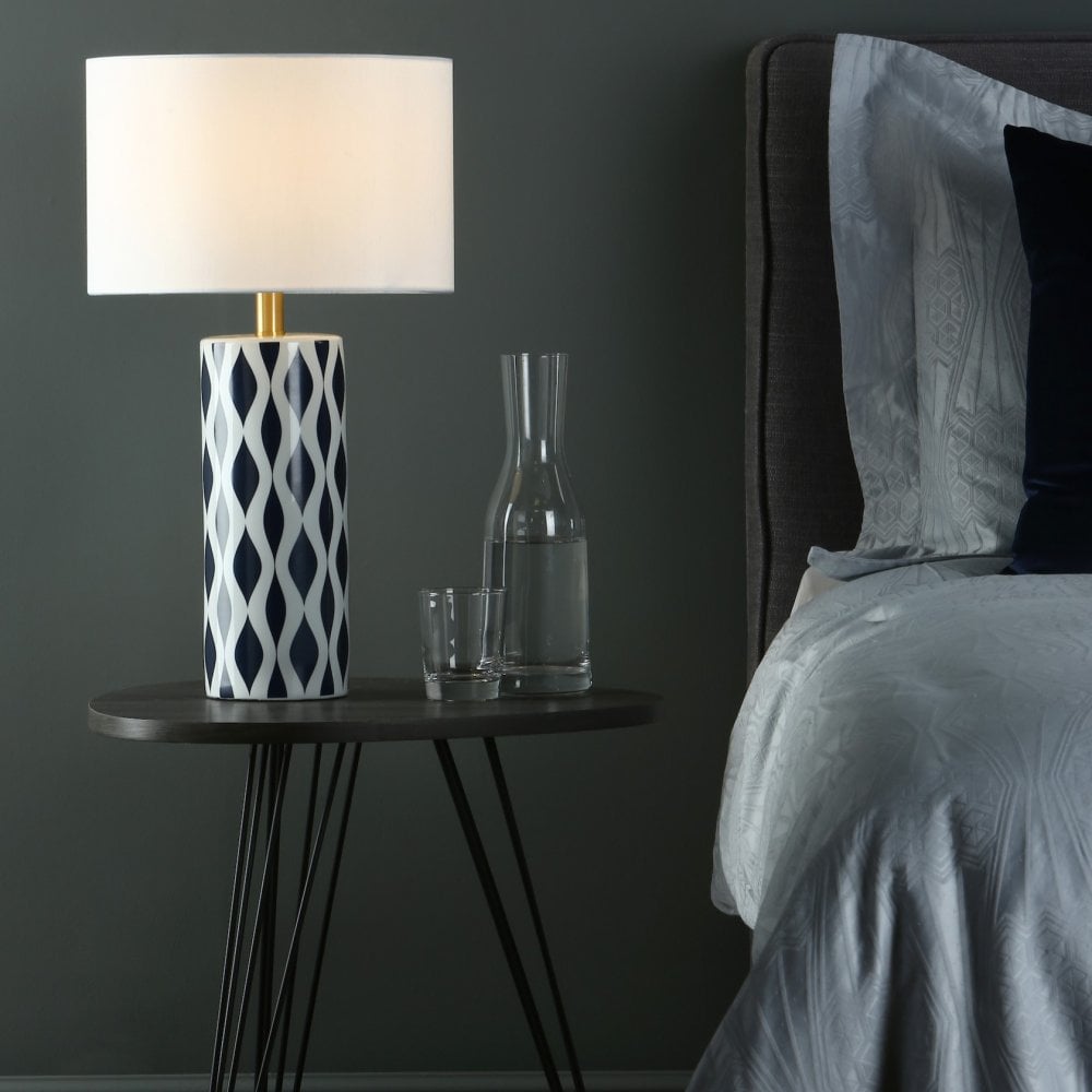 A white table lamp with a dark blue and white patterned base on a bedside table.
