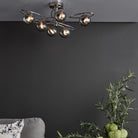 A modern ceiling light with six smoked glass orbs on chrome swirls in a grey living room.