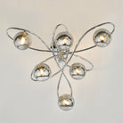 A modern ceiling light with six smoked glass orbs on chrome swirls on a light background.