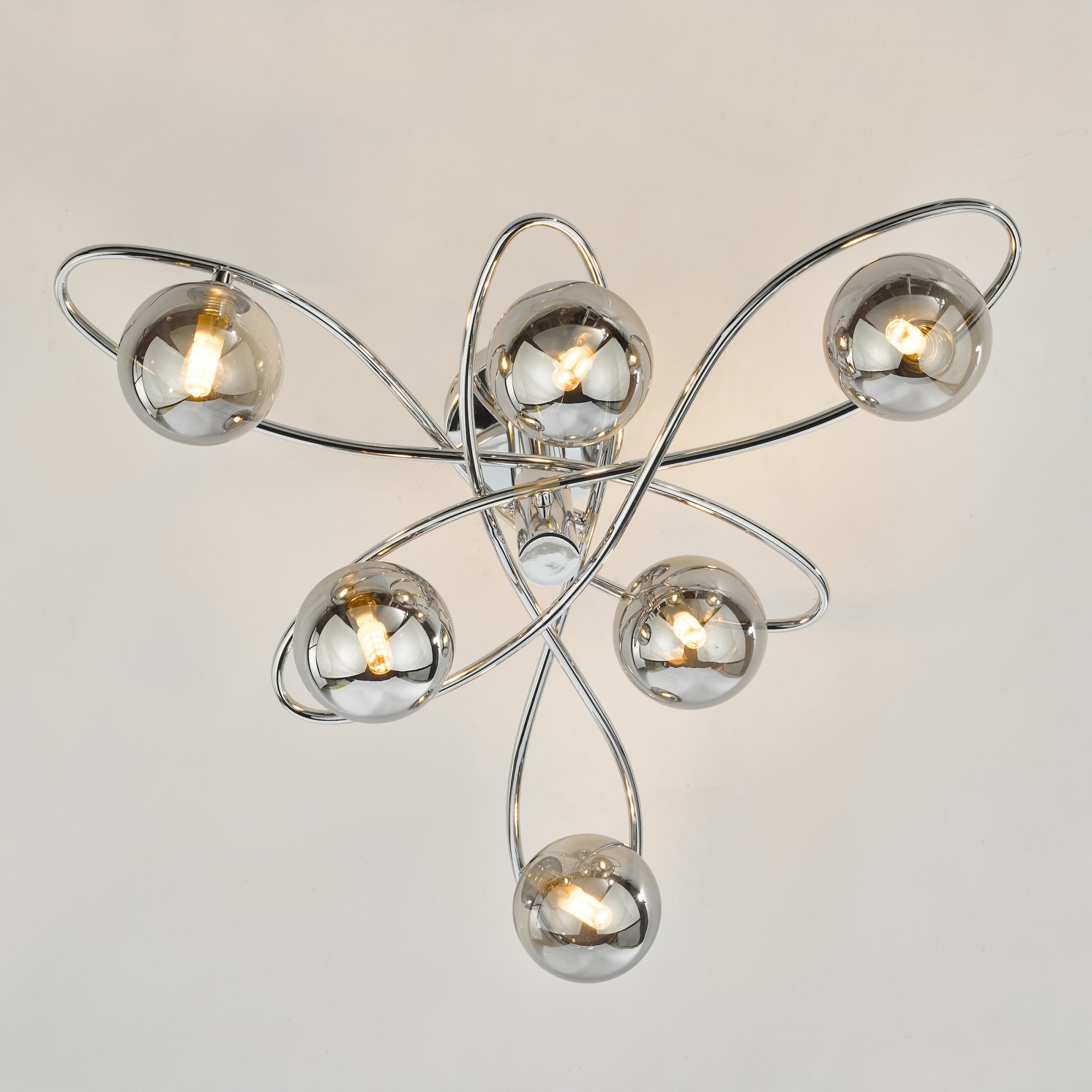 A modern ceiling light with six smoked glass orbs on chrome swirls on a light background.
