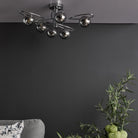 A modern ceiling light with six smoked glass orbs on chrome swirls against a grey wall.