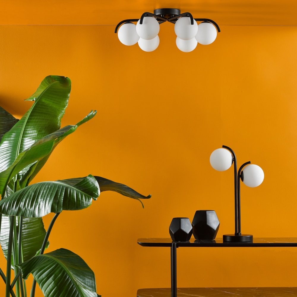 A modern black ceiling light illuminates a room with vibrant orange walls and a lush plant.