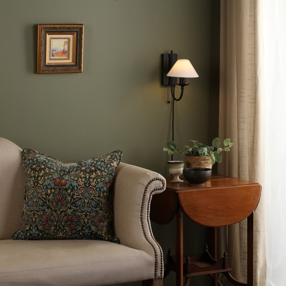 A living room with a green wall, cream sofa, side table, and wall sconce.