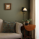 A living room with a green wall, cream sofa, side table, and wall sconce.