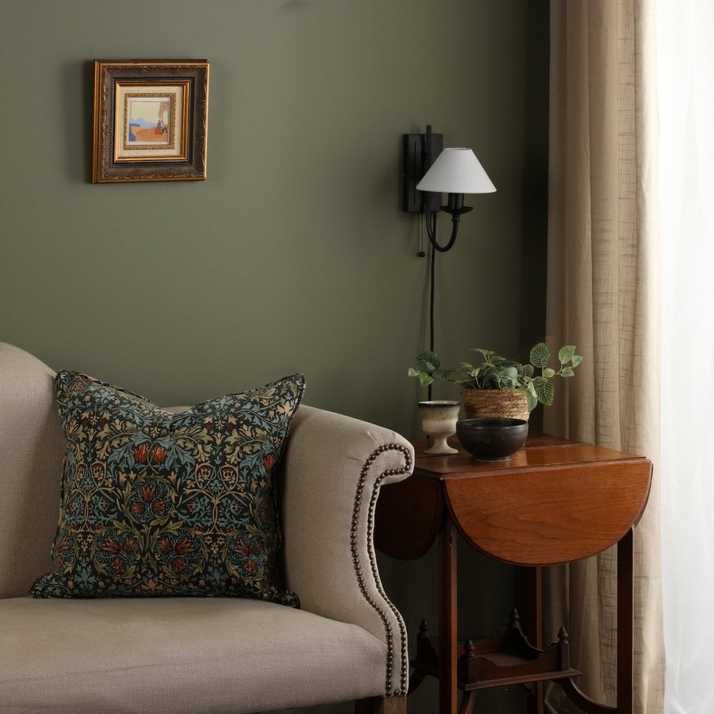 A living room with a green wall, cream sofa, side table, and wall sconce.