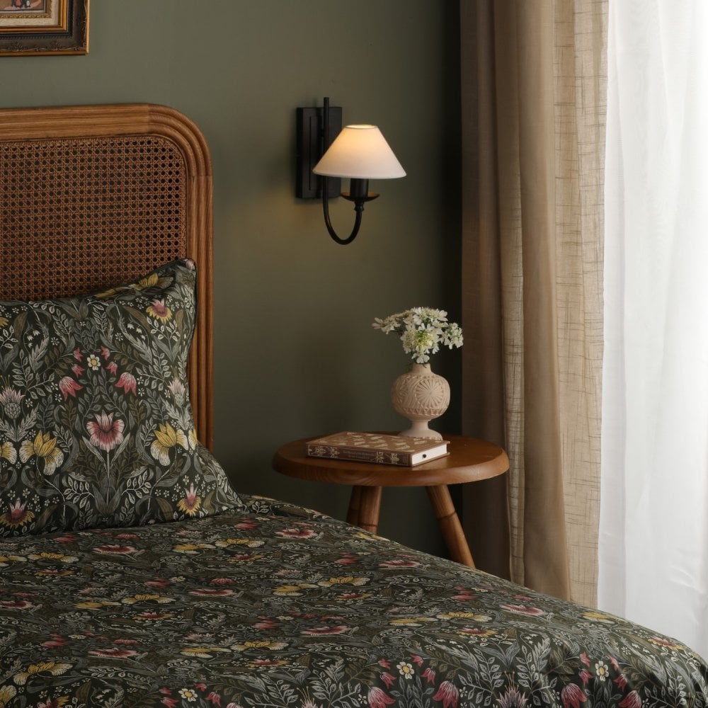 A bedroom with a green wall, rattan headboard, patterned bedding, and wall sconce.