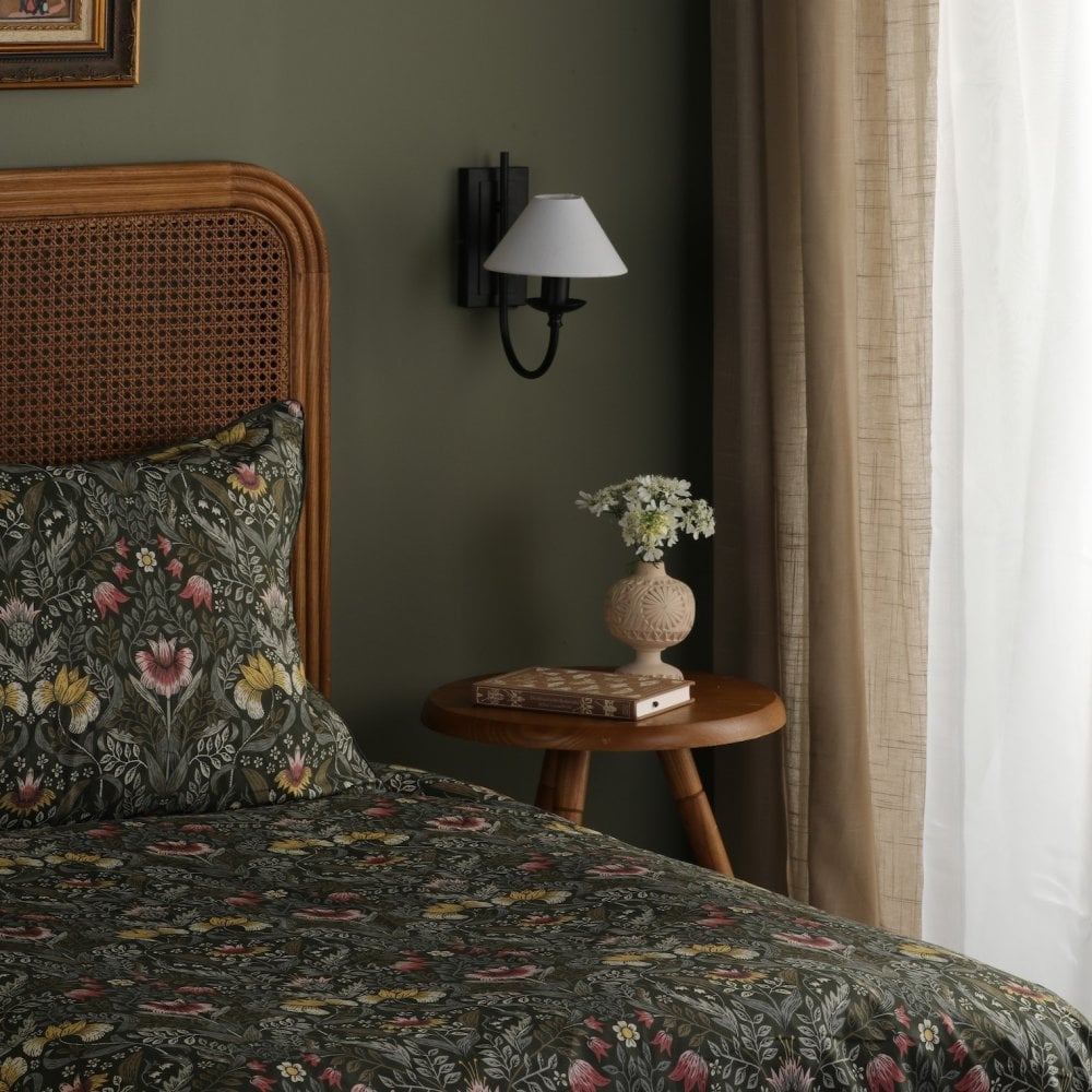 A bedroom with a green wall, rattan headboard, patterned bedding, and wall sconce.