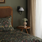 A bedroom with a green wall, rattan headboard, patterned bedding, and wall sconce.