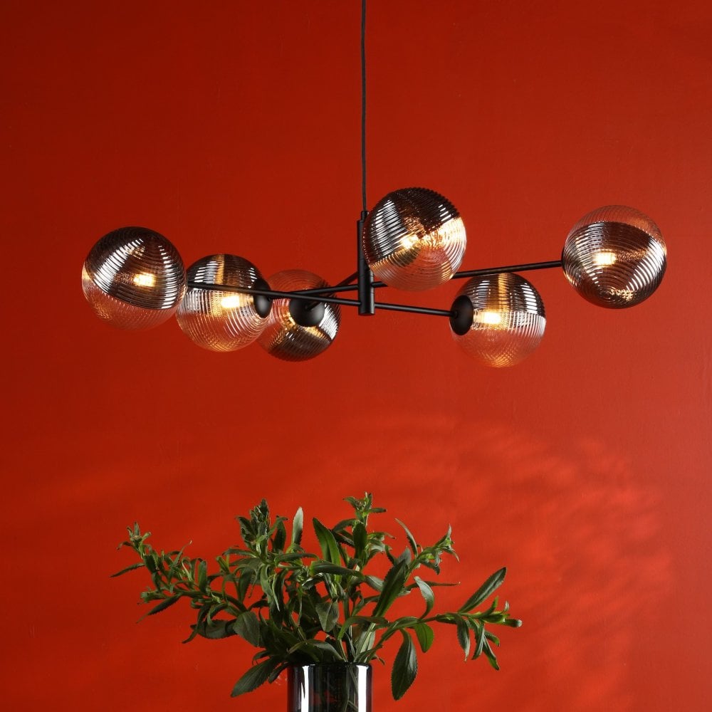 A modern chandelier with six tinted glass globe shades hanging over a plant in a vase.