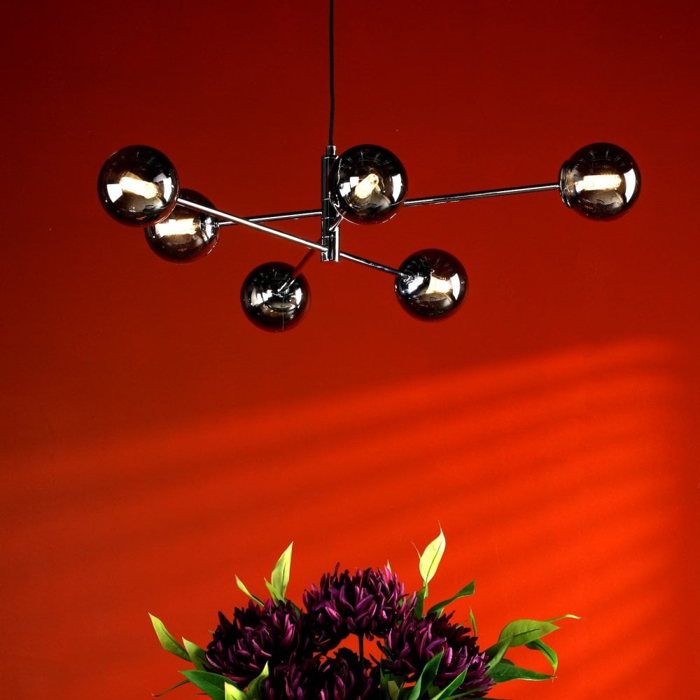 A modern chandelier with six smoked glass globes hangs above a floral arrangement.