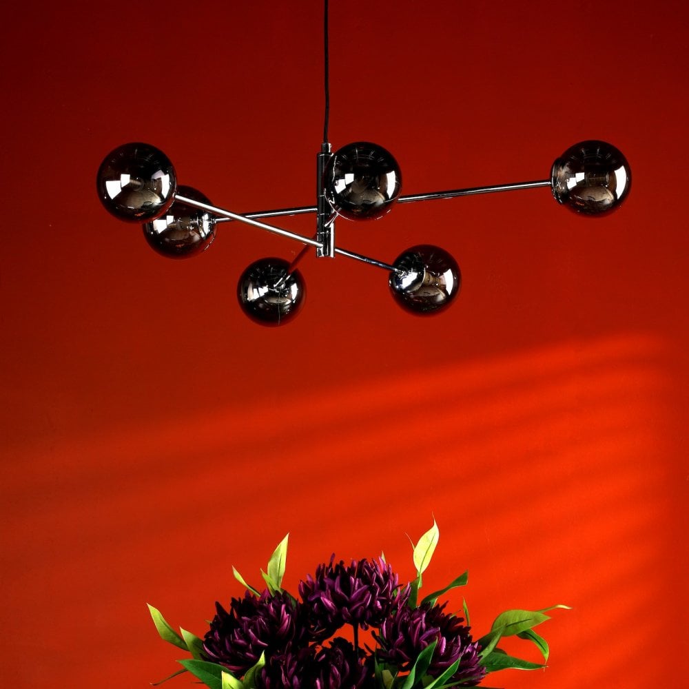 A modern chandelier with six smoked glass globes hangs above a floral arrangement.