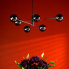 A modern chandelier with six smoked glass globes hangs above a floral arrangement.