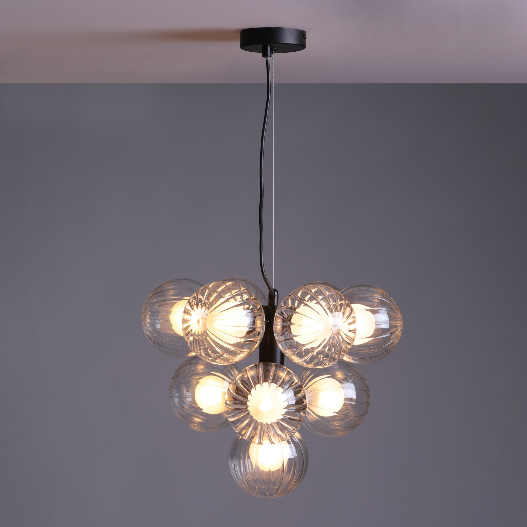 Modern chandelier with seven clear glass globes and a black ceiling mount, on grey.