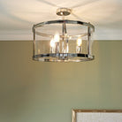 Polished chrome semi-flush ceiling light with clear glass shade, glowing warmly.